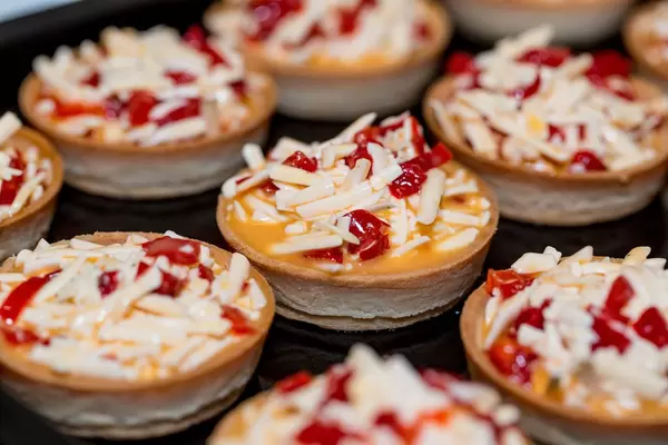 Törtchen mit Gemüse und Käse liegen auf schwarzem Backblech