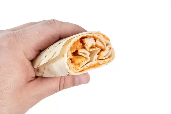 Tortilla mit Hühnchenfleisch mit Gemüse in einer Hand vor weißem Hintergrund