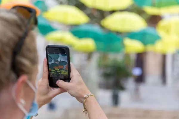 Touristin mit Mundschutz fotografiert bunte Regenschirme in Sóller, Mallorca mit ihrem iPhone