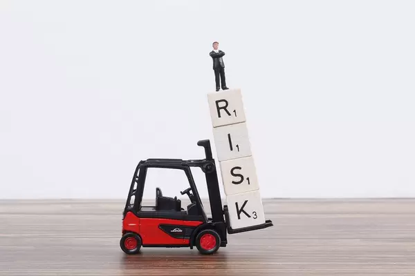 Toy forklift holds wooden blocks with Risk text and businessman