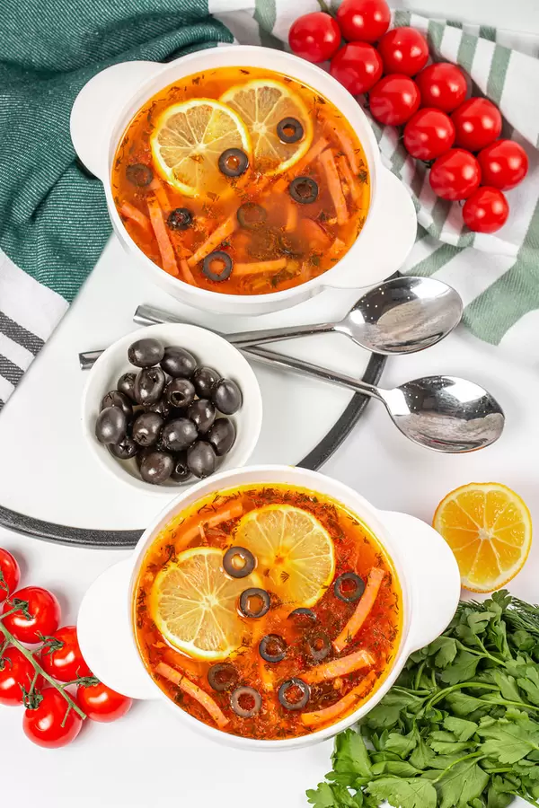 Traditional russian soup solyanka cooked with meat, sausages, lemon, salted cucumbers and olives