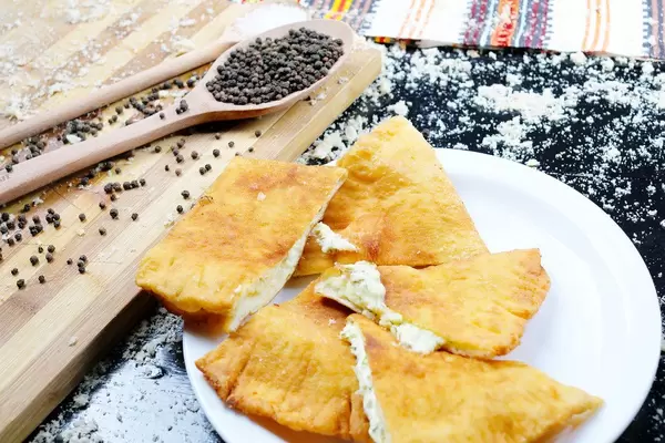 Traditionelles Rezept aus Ungarn: Langos mit Käse auf einem weißen Teller vor schwarzem Hintergrund