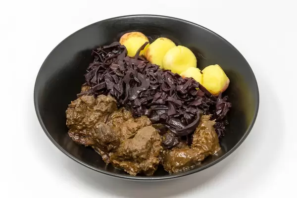 Traditionelles Rindergulasch mit Apfel-Rotkohl und Miniknödeln in einer schwarzen Schüssel
