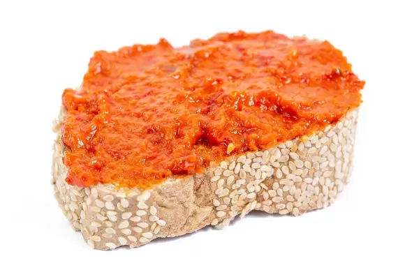 Traditionelles serbisches Ajvar-Mus als Brotaufstrich auf einem Weißbrot vor weißem Hintergrund