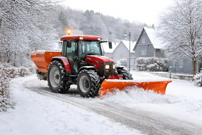 Traktor räumt verschneite Straße in winterlicher Landschaft