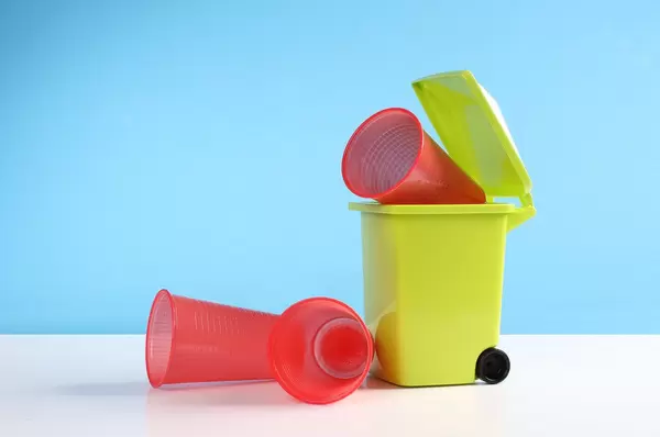 Trash bin with a plastic cups on blue background