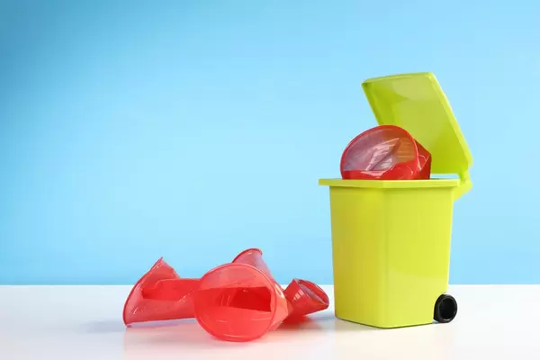 Trash bin with red plastic cups on blue background