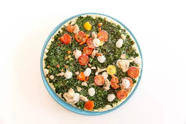 Trattoria Alfredo's vegane pizza "Verdura" mit Spinat, Tomaten und Pilzen, angebacken auf einem blauen Teller