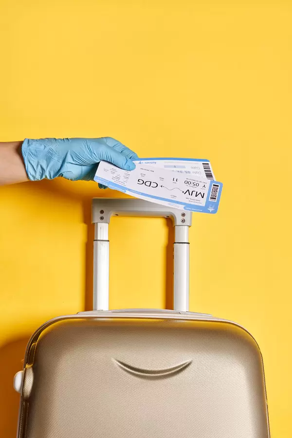 Traveling during coronavirus pandemic - a person with travel luggage holds air flight tickets