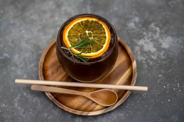 Trendgetränk Cold Brew Kaffee auf einem Holzuntersetzer mit Holzlöffel und Papierstrohhalm