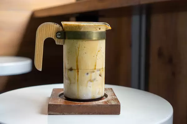 Trendgetränk Dalgona Kaffee in einem Designer Kaffeeglas mit Holzhenkel auf einem Holz-Untersetzer