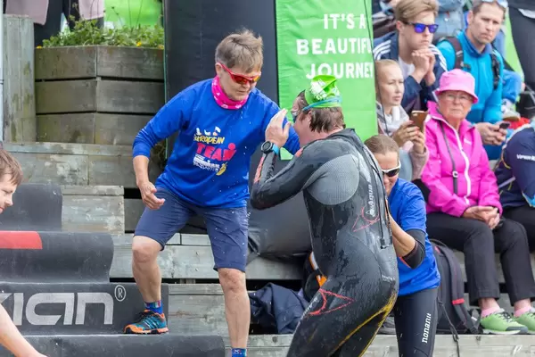 Triathleten in Neoprenanzug werden vom Veranstaltungsteam zur nächsten Ironman-Disziplin begleitet