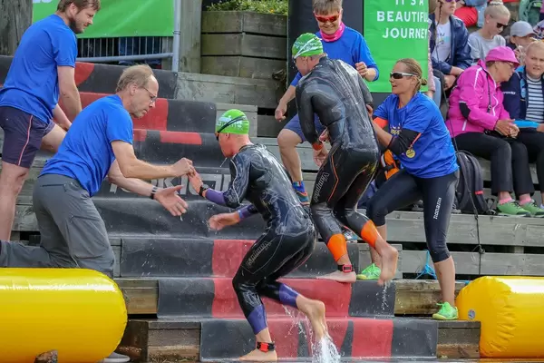 Triathleten rennen nach dem Schwimmwettkampf eine Holztreppe hoch