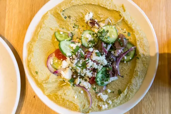 True Food Kitchen's vegetarian herb hummus with cucumber, organic tomato, onion, olive, feta, lemon oregano vinaigrette & house-made pita, on a plate seen from above