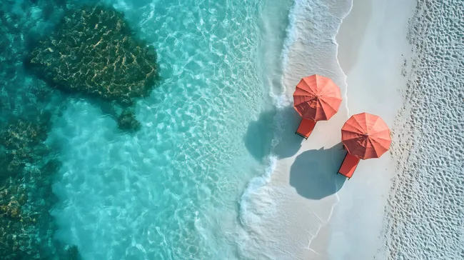 Türkisfarbenes Meer trifft auf weißen Sandstrand mit roten Sonnenschirmen