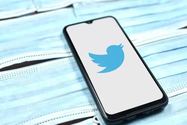 Twitter logo on smartphone screen over the face masks. Global company during coronavirus crisis