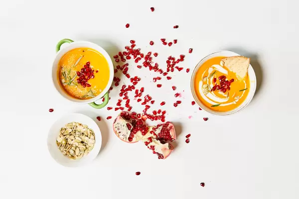 Two bowls of creamy pumpkin soup with pomegranate seeds