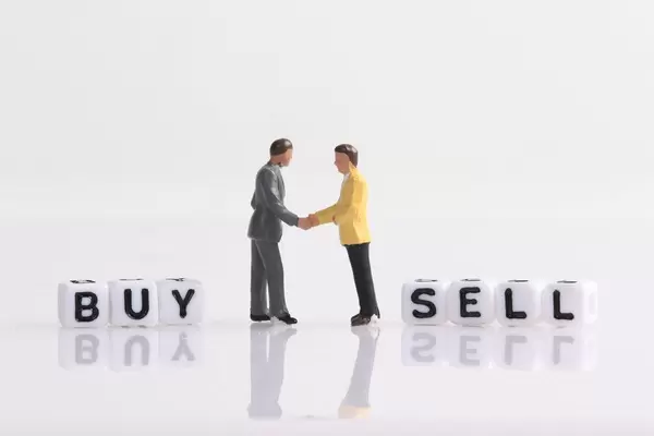 Two businessman shaking hands in front of Buy and Sell text