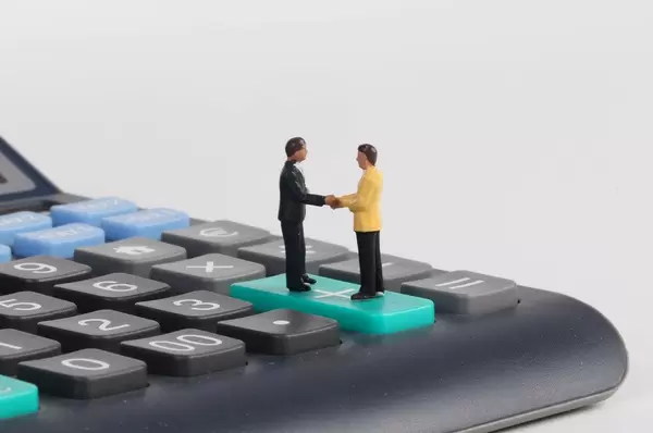 Two businessman shaking hands while standing on calculator