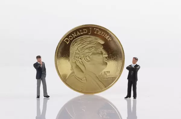 Two businessman standing next to a golden Donald Trump coin