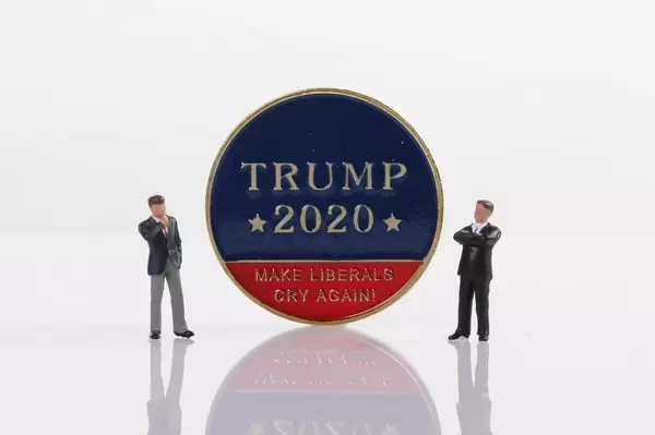 Two businessman standing next to a Trump 2020 golden coin