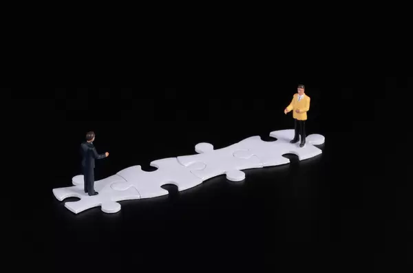 Two businessman standing on white puzzle pieces with black background
