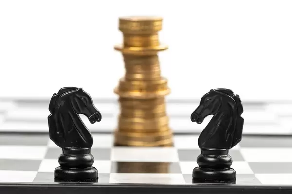 Two chess horses on a chessboard and a king of coins in the background, business and money concept