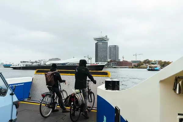 Two commuters on bicycles taking a ferry across a canal in Amsterdam
