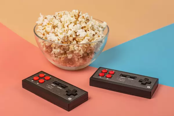 Two consoles for an eight-bit computer game with a bowl of popcorn on a colorful background