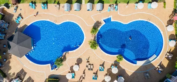 Two eight-form pools with sun beds and parasols. Overhead drone shot near Cala Mesquida, Mallorca