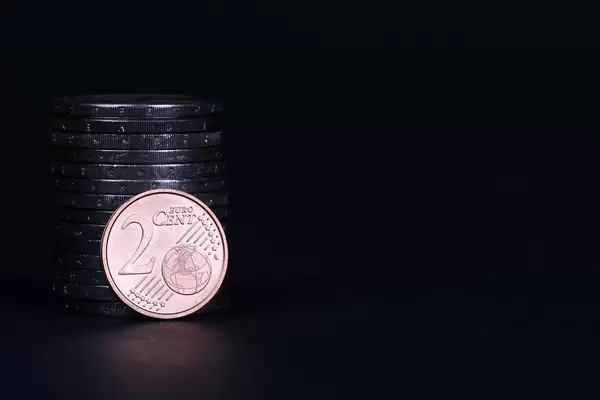Two Euro cent coin placed in front of piles of coins on black background
