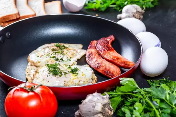 Two fried chicken eggs in a frying pan with sausages on a black background