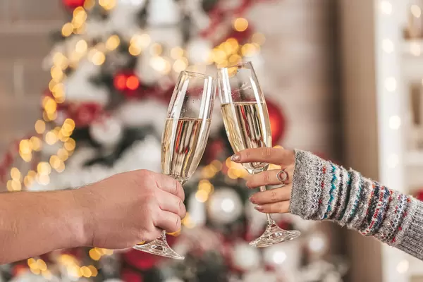 Two glasses of champagne in the hands of a man and a woman on a blurred background of a decorated christmas tree