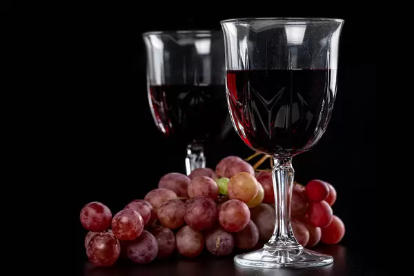 Two glasses of wine with a branch of fresh grapes on a dark background
