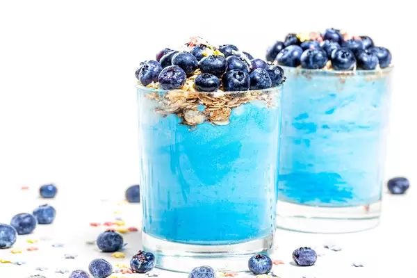 Two glasses with fresh blue smoothies and blueberries