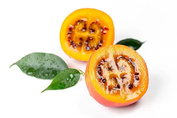 Two halves of ripe juicy tamarillo with leaves on a white background (Flip 2020)