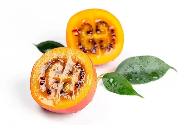 Two halves of ripe juicy tamarillo with leaves on a white background