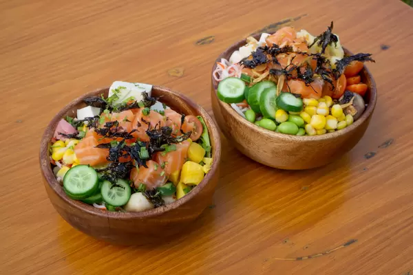 Two Healthy Poke Bowls with different fresh Vegetables, Tofu, Fried Onions, Salmon and Dried Seaweed in Wooden Bowls