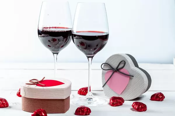 Two Heart Shaped Boxes with Pralines and Two Wine Glasses with Red Wine in the Background for Valentines Day