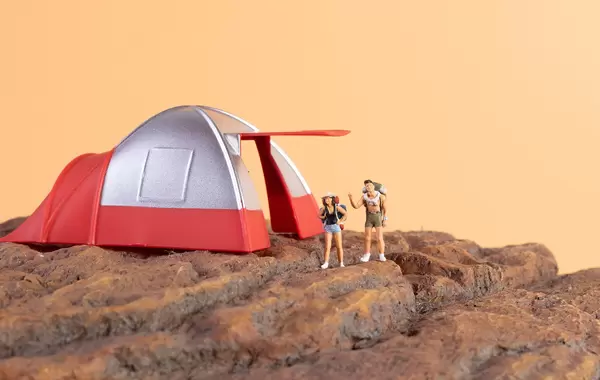 Two hikers standing on rocks and camping tent