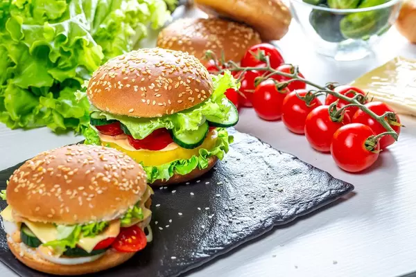 Two homemade hamburgers with fresh vegetables on black stone tray (Flip 2019)