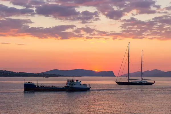Two-master sailboat and a cargo boat on the sea, with sunset and cloudy red sky in the background