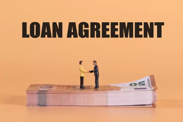 Two miniature businessman shaking hands on a stack of Euro money with Loan Agreement text
