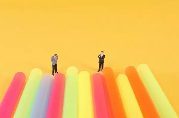 Two miniature businessman standing next to colorful drinking straws