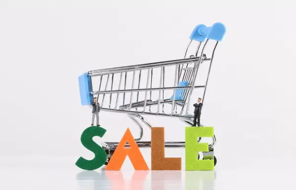 Two miniature businessman with shopping cart and Sale text on white background