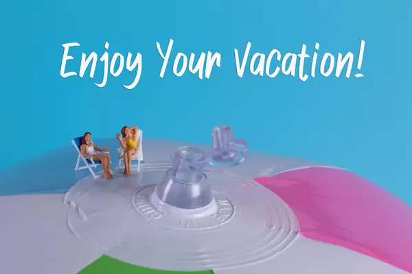 Two miniature girls in swimsuit sitting on a beach ball with Enjoy Your Vacation text