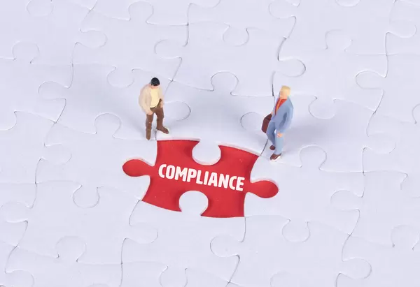 Two miniature man looking at a missing puzzle piece with Compliance text