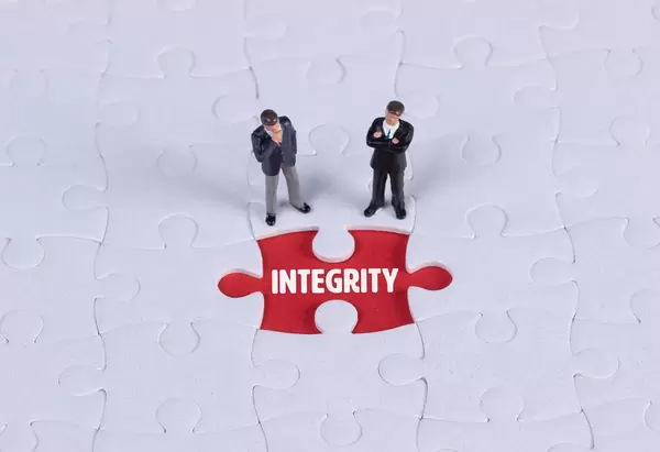 Two miniature man looking at a missing puzzle piece with Integrity text