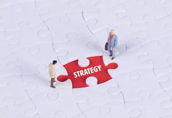 Two miniature man looking at a missing puzzle piece with Strategy text
