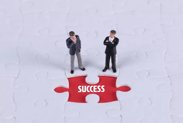 Two miniature man looking at a missing puzzle piece with Success text